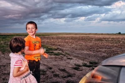 Children standing on landscape against cloudy sky