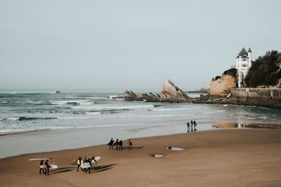 People with surfboards at beach against sky