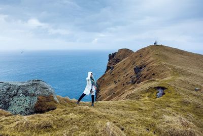 Woman standing on cliff by sea against cloudy sky