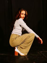 Portrait of young woman crouching against black background