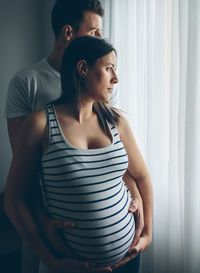 Pregnant woman with husband standing by window at home