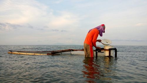 Fisherman holding container in sea against sky