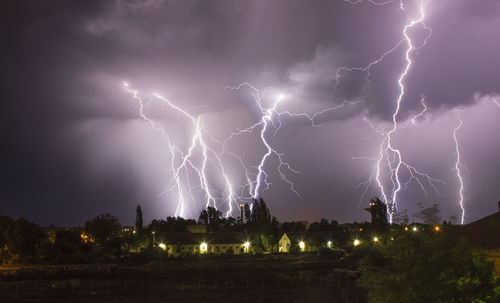 Low angle view of lightning over houses at dusk