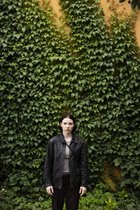 Portrait of young woman standing in front of hedge at park