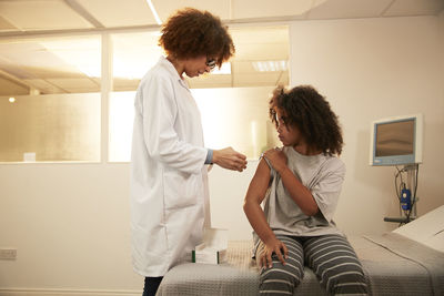 Doctor standing by patient sitting on bed in medical room at hospital