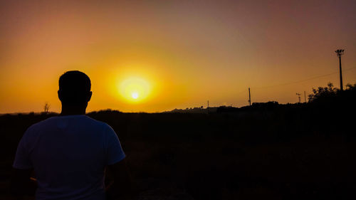 Silhouette man standing on landscape against orange sky