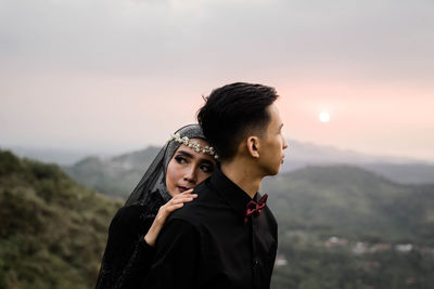 Young couple standing on mountain against sky