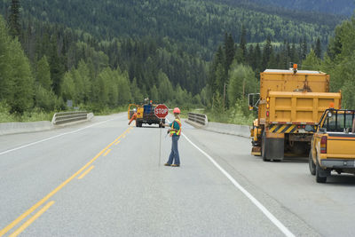 Manual worker with stop sign on road against trees