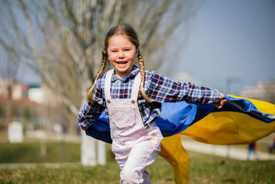 Portrait of girl running with ukrainian flag against sky