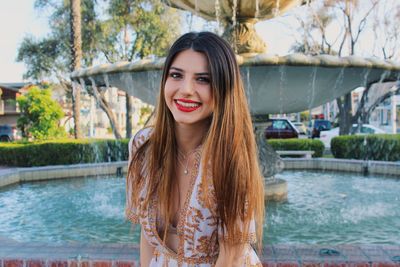 Portrait of smiling young woman standing against fountain