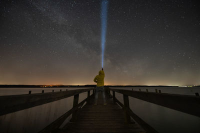 Rear view of man standing on pier against sky at night