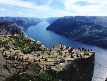 High angle view of people on cliff by lake against sky