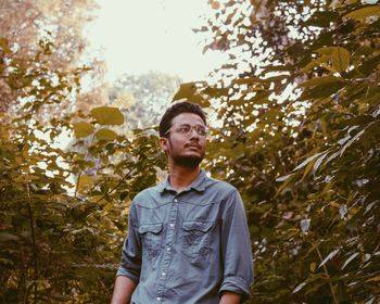 Portrait of young man looking away against trees