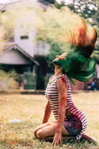 Woman splashing powder paint with hair while sitting on field