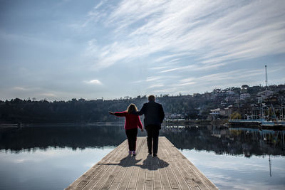 Rear view of women standing on pier over lake against sky
