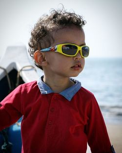 Close-up of boy wearing sunglasses standing against sea