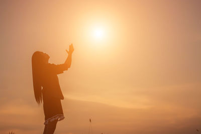 Silhouette man with arms raised against orange sky