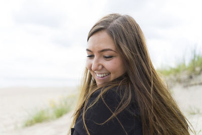 Smiling young woman at beach against sky
