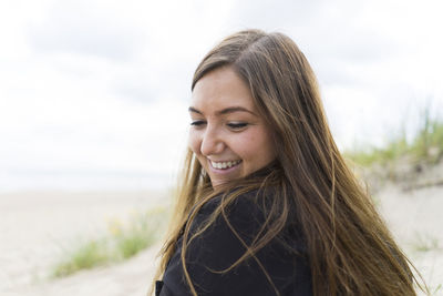 Portrait of smiling young woman at beach against sky