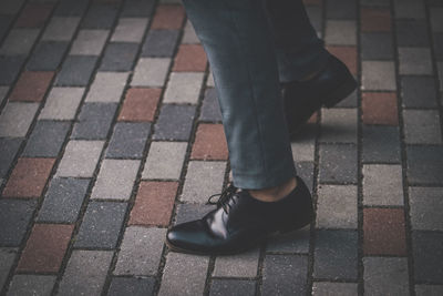Low section of businessman wearing shoes while standing on footpath