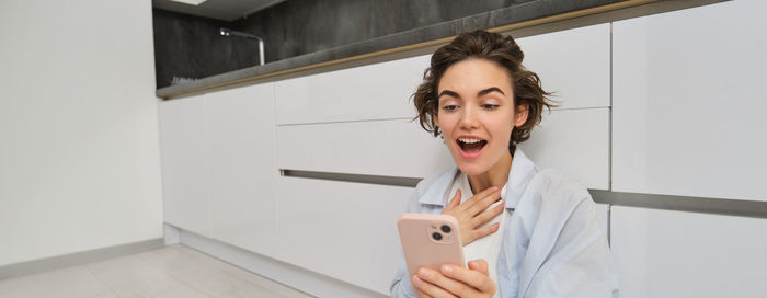 Young woman using mobile phone while standing against wall