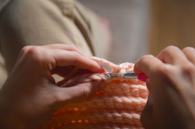 The hands of a young caucasian woman are knitting a woolen product indoors. the concept of hobby and