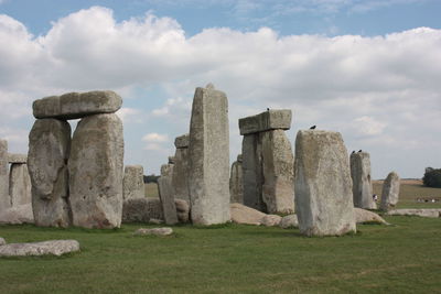 Stone structure in field against cloudy sky