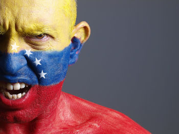 Close-up portrait of angry man with venezuelan flag body paint against gray background