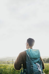 Rear view of man with backpack hiking under sky