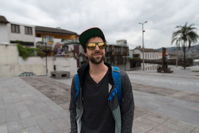 Portrait of young man standing in city against sky