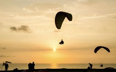 Low angle view of silhouette people paragliding over sea against sky during sunset