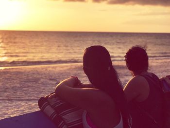 Low section of people sitting on shore against sunset sky