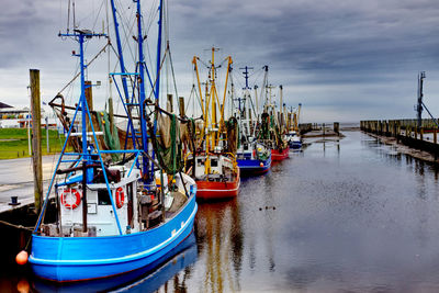 Fishing boats moored at harbor against sky