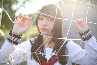 Portrait of young woman standing by sports net