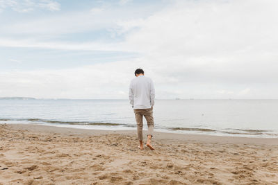 Rear view of man standing on beach against sky