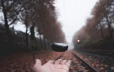 Cropped image of man levitating rock on hand at railroad track