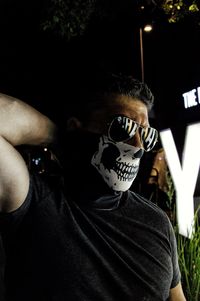 Close-up of man wearing sunglasses and skull mask at night