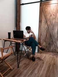 Full length of man using mobile phone while sitting on wooden table