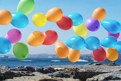 Multi colored balloons on rocks by sea against sky