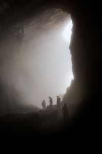 Silhouette friends standing in cave during foggy weather