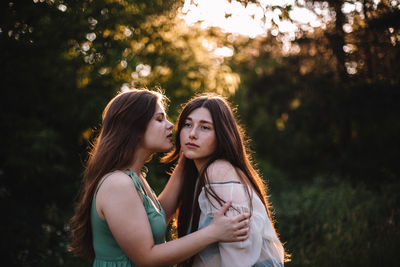 Young woman is about to kiss her girlfriend in forest during summer