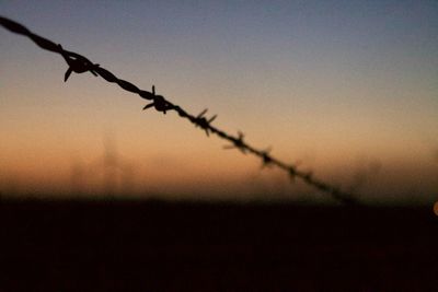 Close-up of silhouette barbed wire against sky at sunset