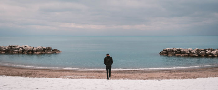 Rear view of man walking at beach against sky