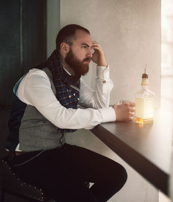 Side view of thoughtful bearded man with drink sitting at home