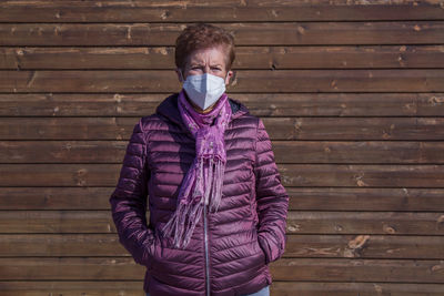 Senior woman with medical mask on face in prevention of coronavirus with wall background