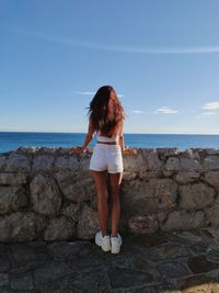 Rear view of woman standing on rock by sea against sky