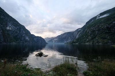 Scenic view of sea by mountains against cloudy sky