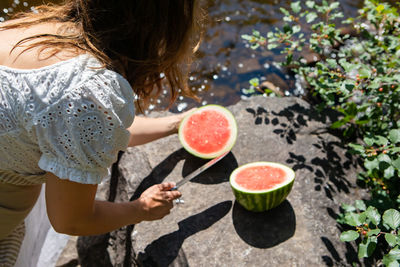 High angle view of woman cutting watermelon by river