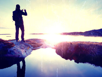 Reflection of man photographing on lake against sky