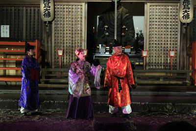 Rear view of people walking on sidewalk in city at night